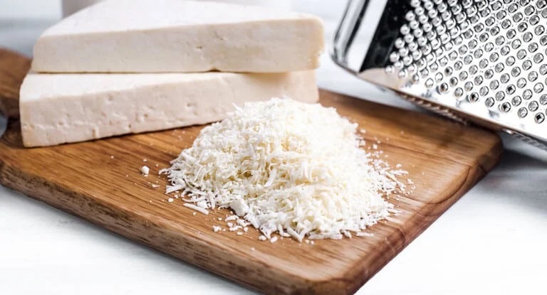Some grated Cotija cheese next to two pieces of Cotija mold cheese